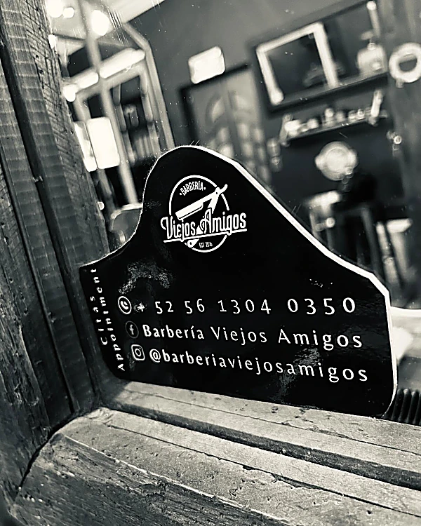 Letrero negro con el logo de Barbería Viejos Amigos, Est. 2016, y el teléfono de citas 56 1304 0350