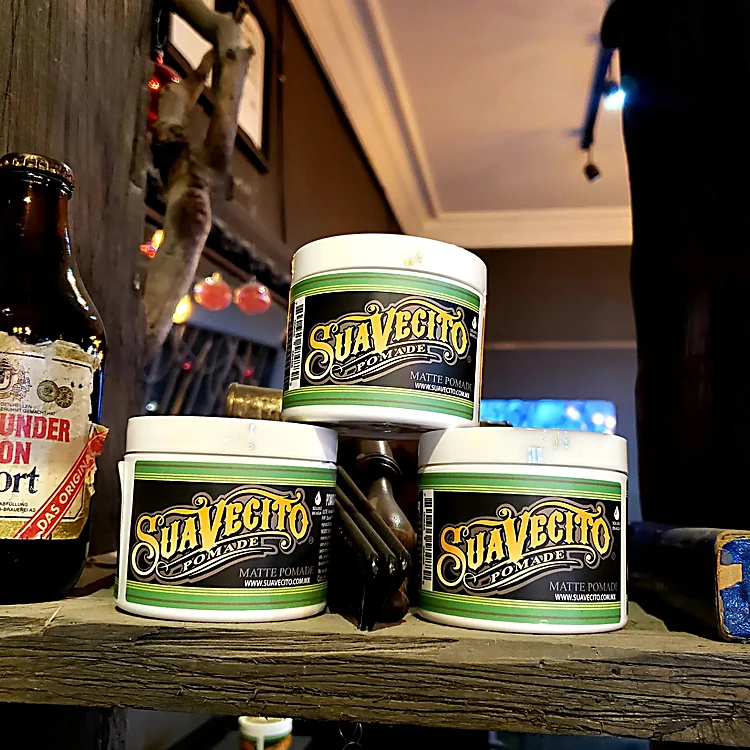Latas de pomada Suavecito apiladas sobre una repisa