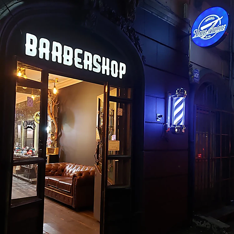Puerta del local anterior de noche, con el letrero Barbershop y un poste de barbero encendido
